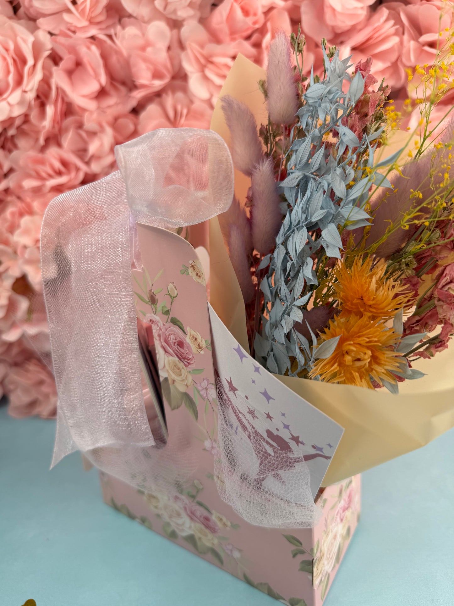 Bouquet of flowers in a decorative box with a pink floral design on a light blue background.