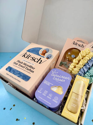 Kitsch beauty products including a towel, sunscreen eraser, and serum in a box on a blue background.