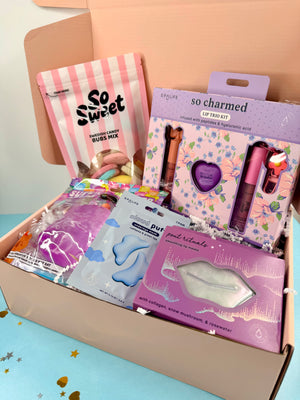 Open box containing various beauty products with visible branding on a light blue surface.