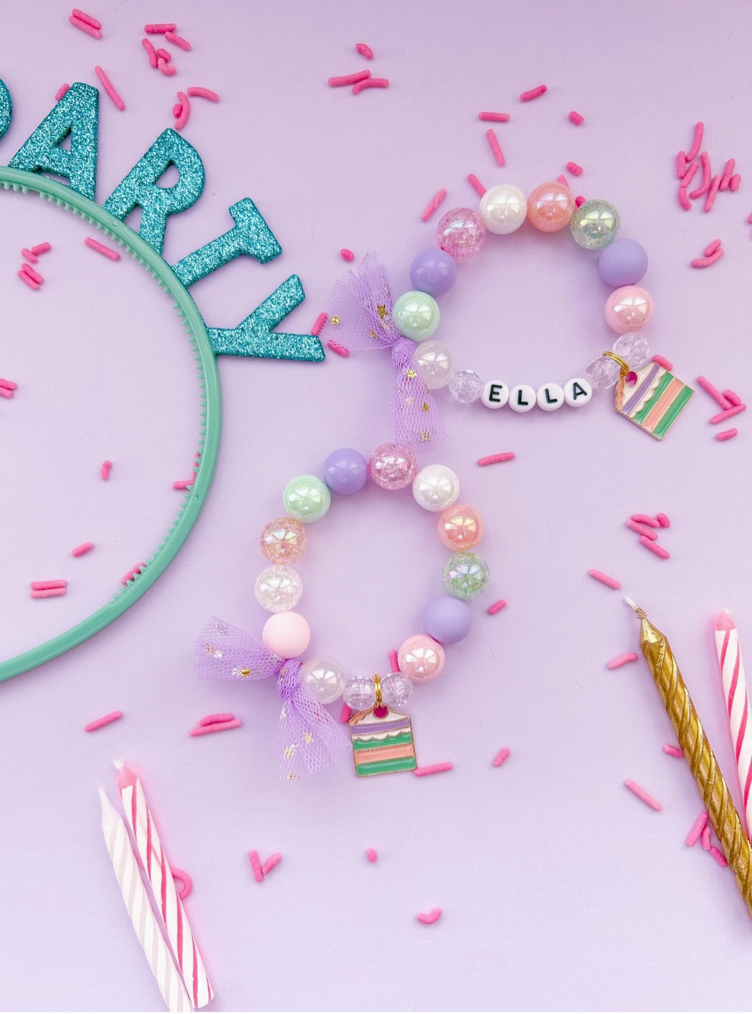 A colorful birthday girl charm bracelet made with acrylic beads and a name charm, displayed on a pink background with party decorations.