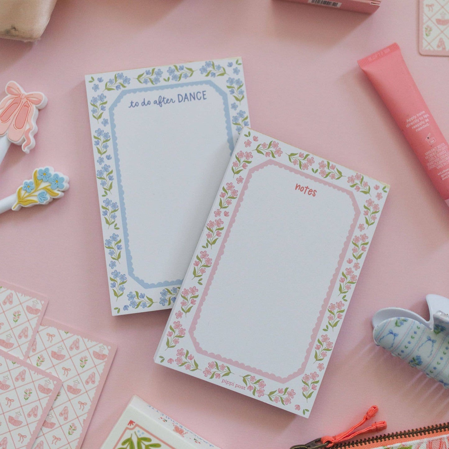 Two floral notepads with writing prompts, styled on a pink background with stationery props.