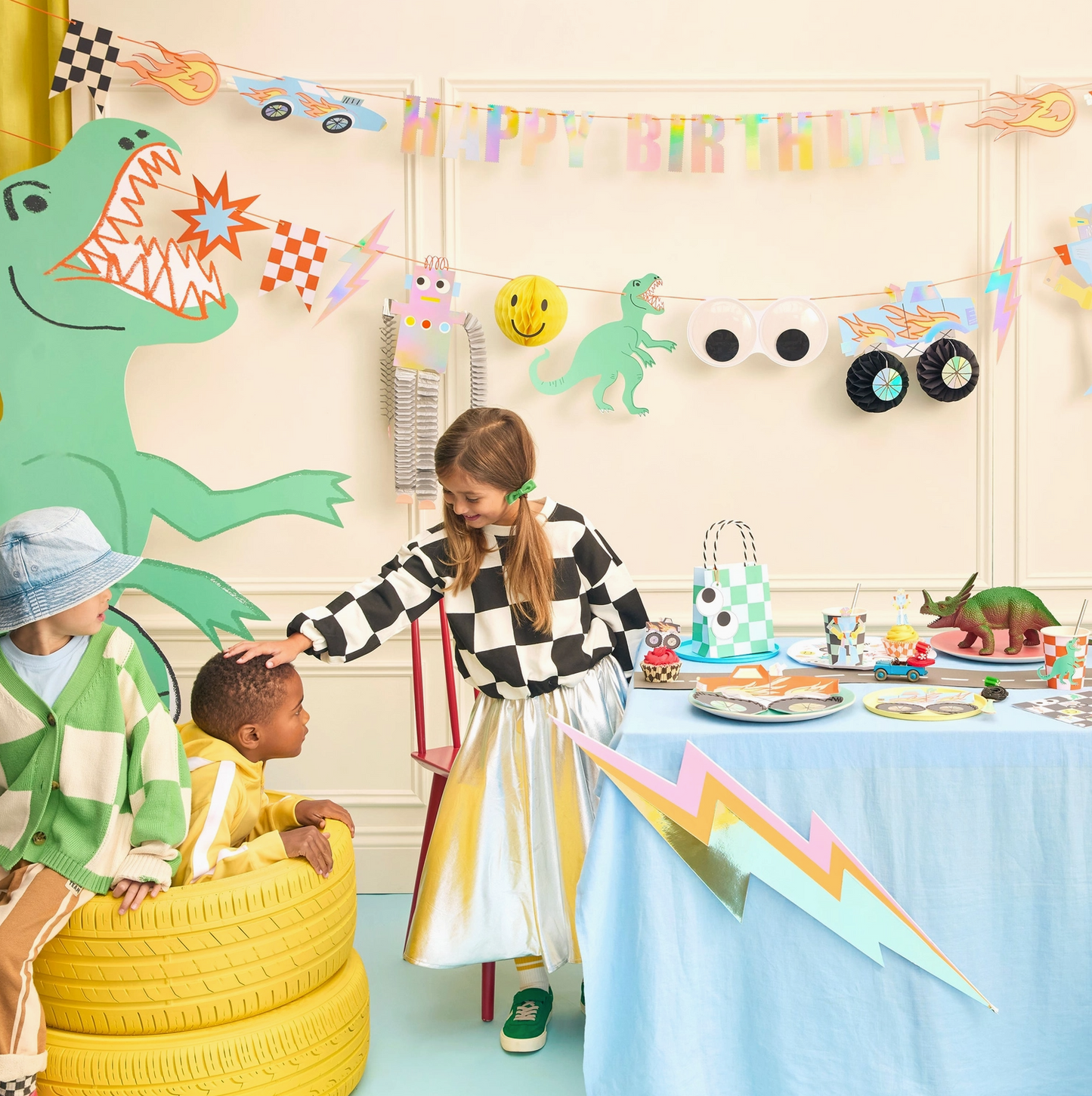 Children at a birthday party with dinosaur-themed decorations and a 'Happy Birthday' banner.