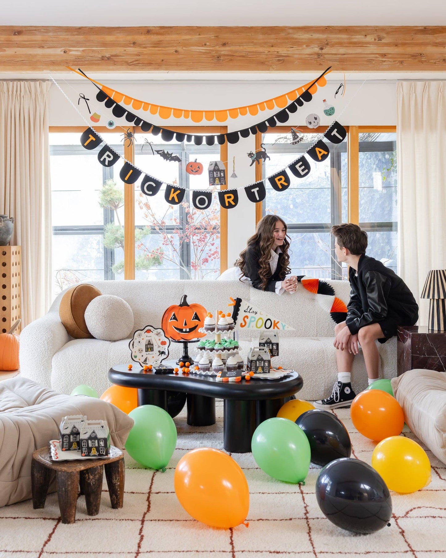 Living room decorated for Halloween with balloons, a banner, and people sitting on a couch.