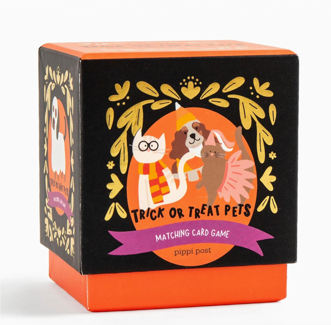 The product packaging for the 'Trick or Treat Pets' Matching Card Game by Pippi Post. The box is a cube-shaped black container with a bright orange base and top, decorated with a festive illustration of a cat and a dog in Halloween costumes surrounded by gold leaves.