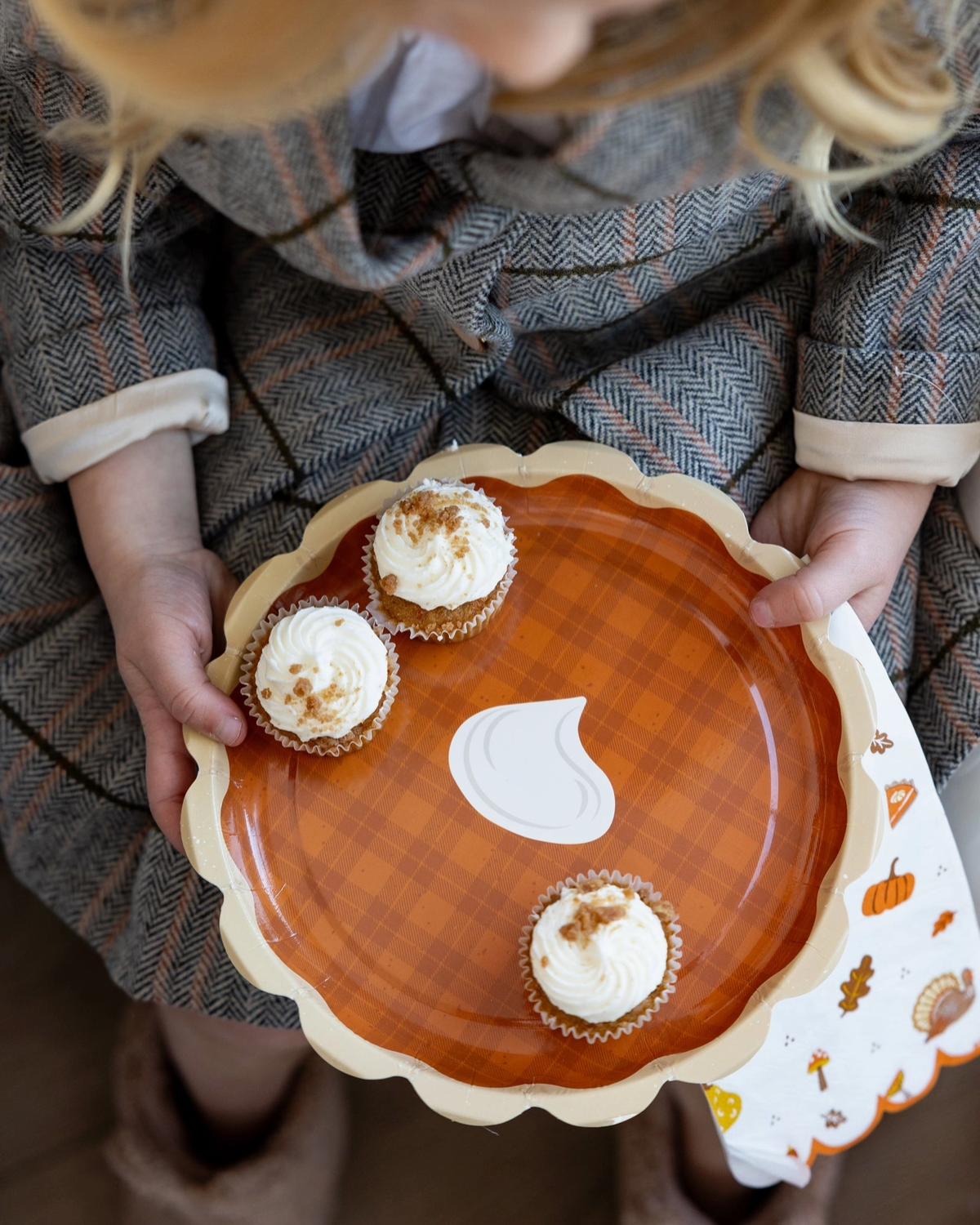 Child holding a decorative plate with a pumpkin design and cupcakes.