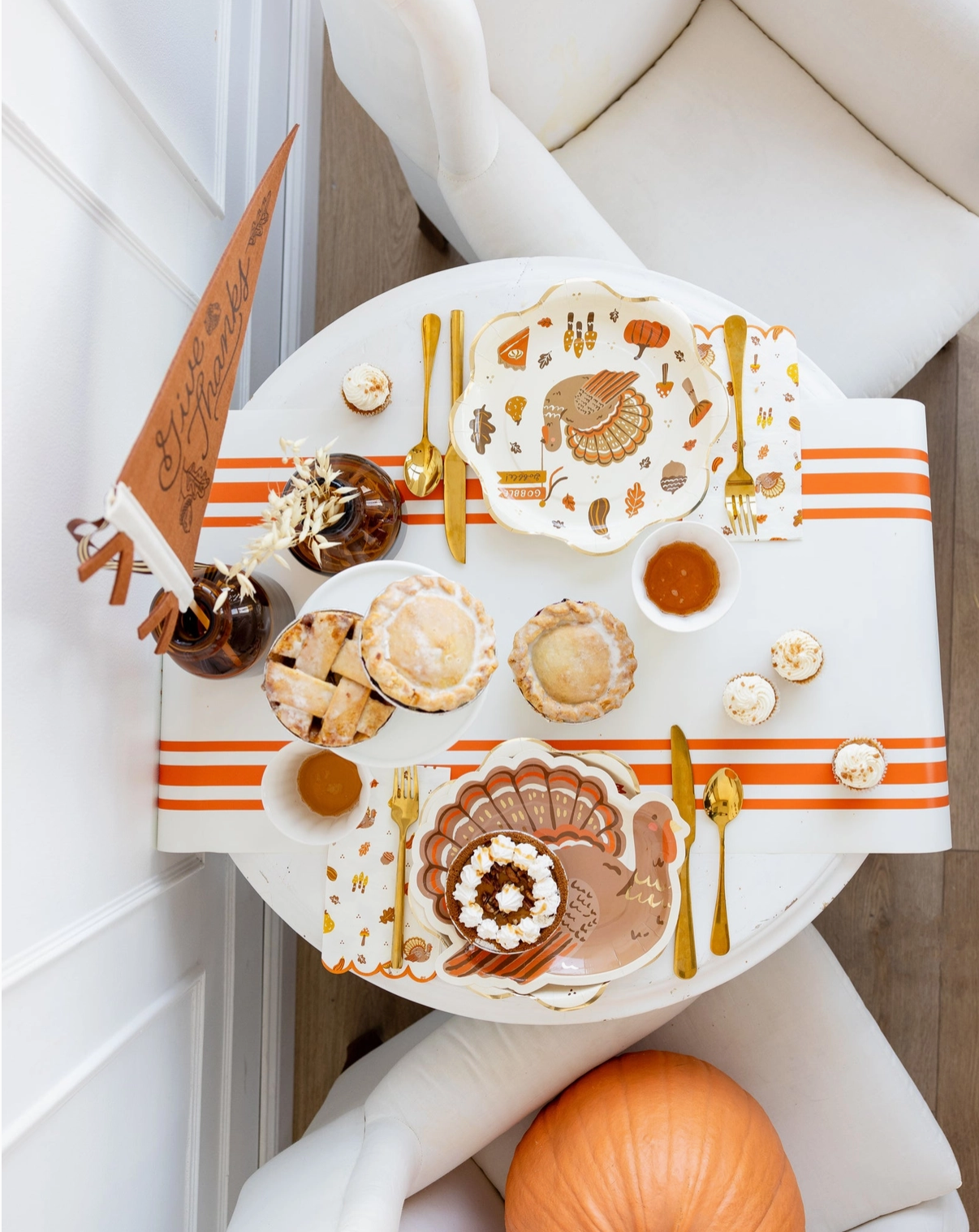Decorative table setting with Thanksgiving-themed plates, napkins, and cutlery on a white surface.