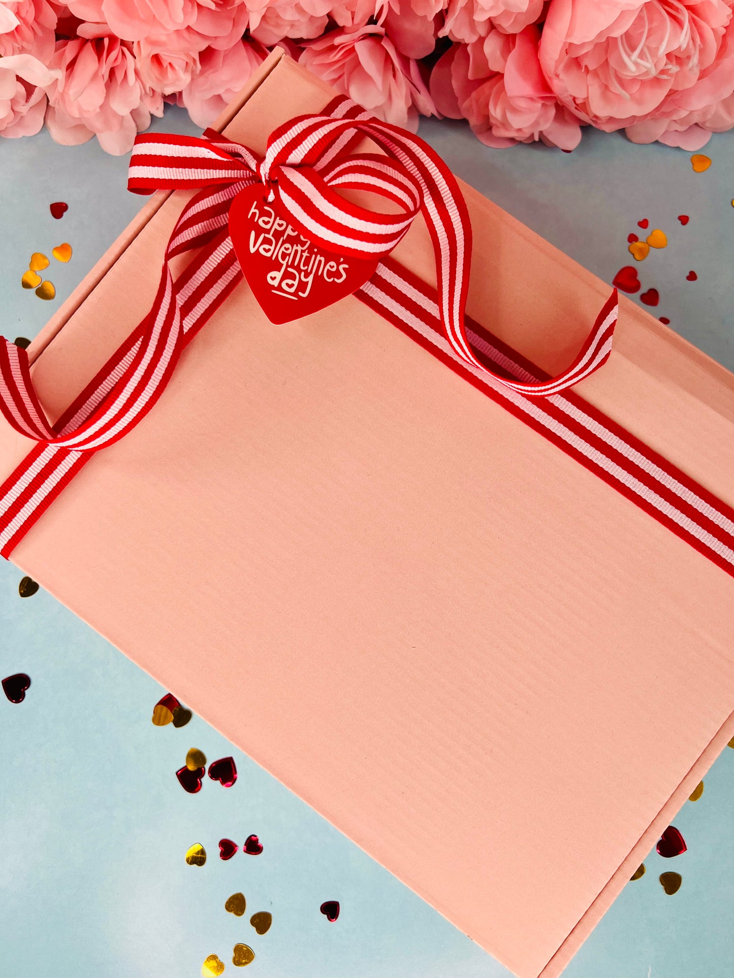 Gift box with a red and white striped ribbon and heart-shaped tag on a light blue background with pink flowers.