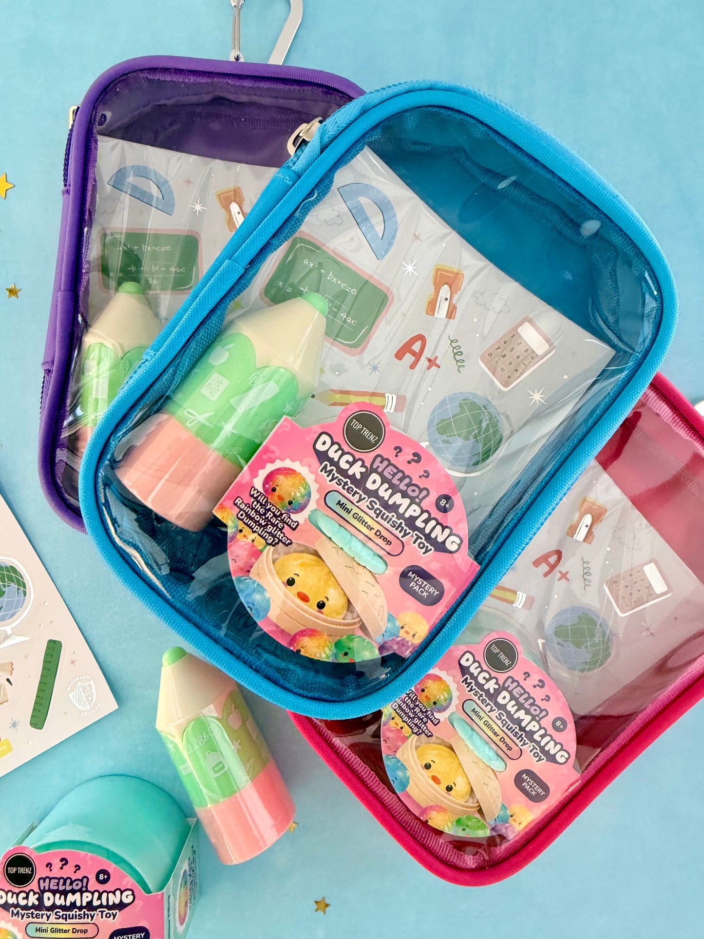 Three colorful zippered pouches in purple, blue, and pink, filled with school supplies and a pack of 'Owl Dimpings' novelty toys, arranged on a light blue background.
