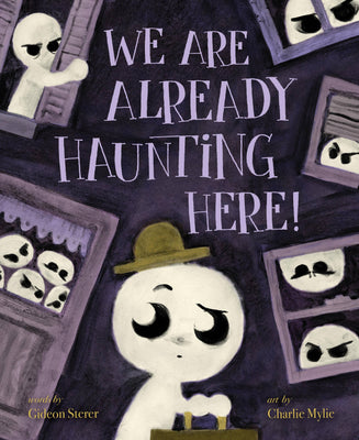 Children's book cover titled 'WE ARE ALREADY HAUNTING HERE!' with a stylized white ghost-like character wearing a brown hat at the bottom center, surrounded by dark purple house outlines and creepy faces peeking out from windows. Text at the bottom credits Gideon Sterer and Charlie Mylie.