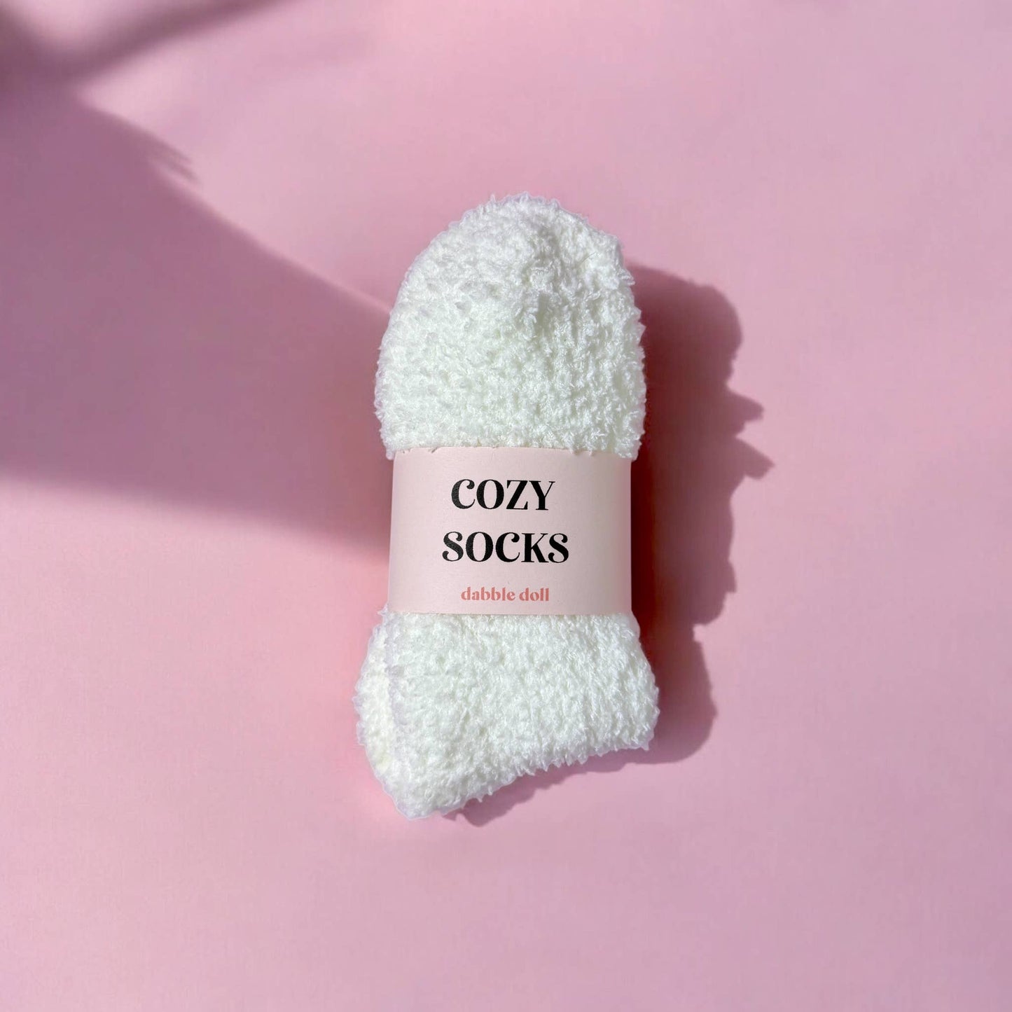 White fluffy sock with 'Cozy Socks' label on a pink background