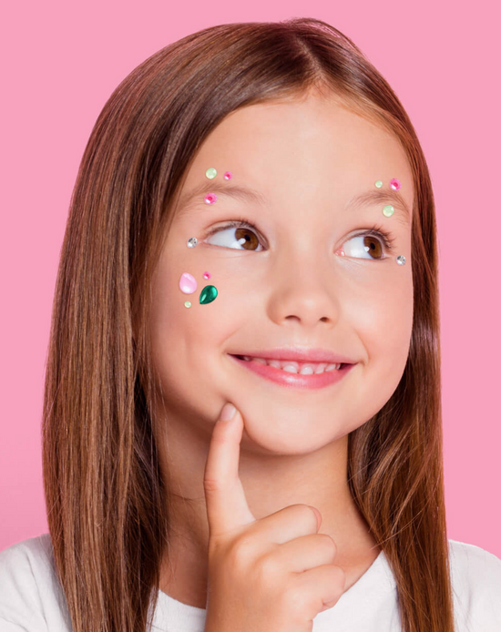 Young girl with decorative stickers on her face against a pink background