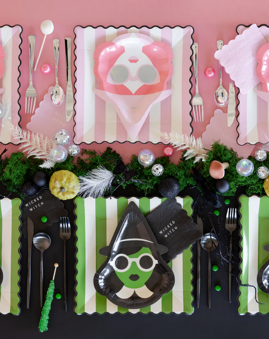 Decorative table setting with witch-themed plates, cutlery, and green accents on a pink background.