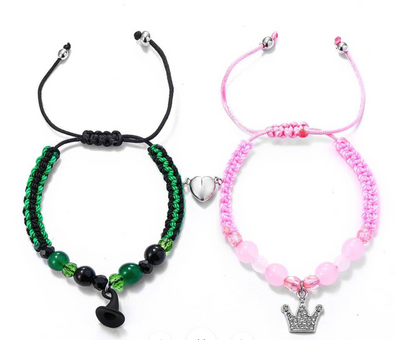 Two bracelets, one green and black with a heart charm, the other pink with a crown charm, on a white background.