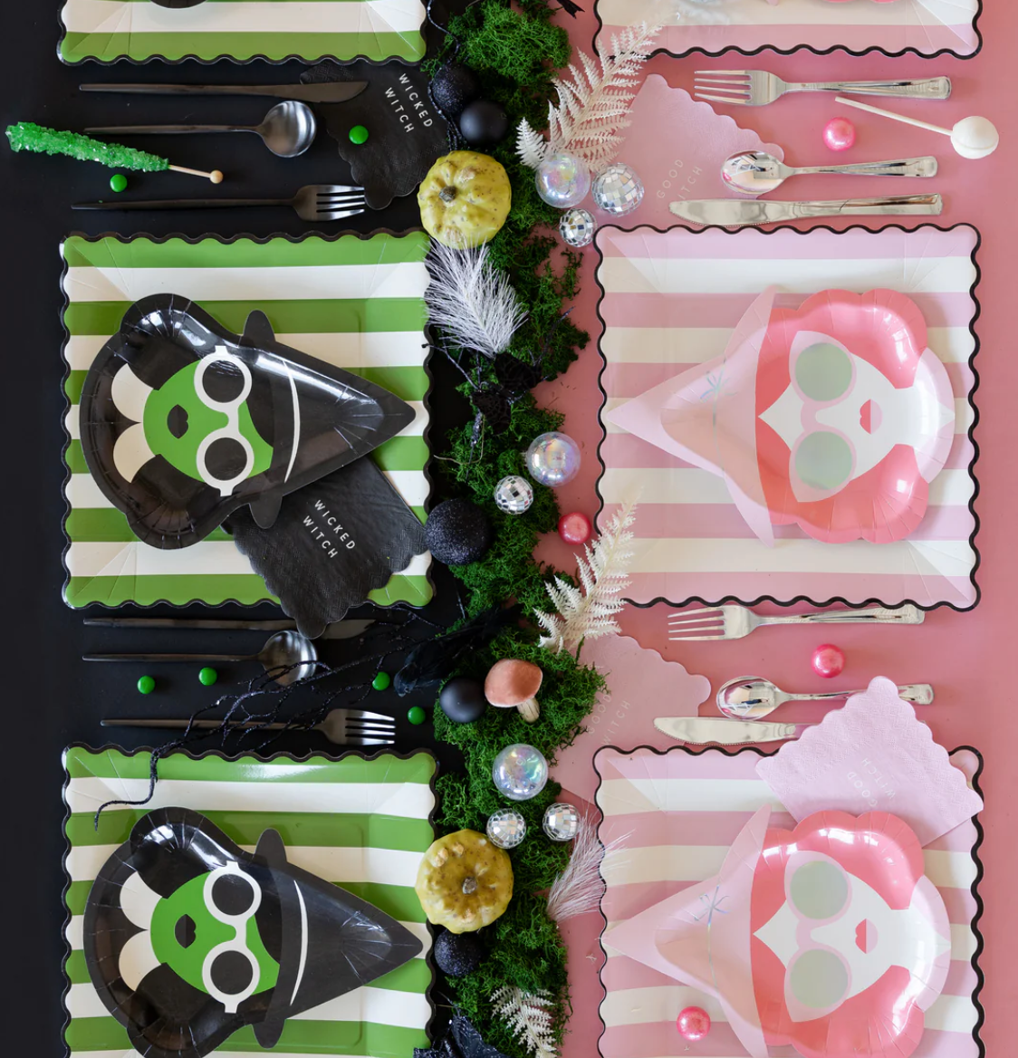 Decorative table setting with Halloween-themed plates, cutlery, and decorations on a pink and green striped background.