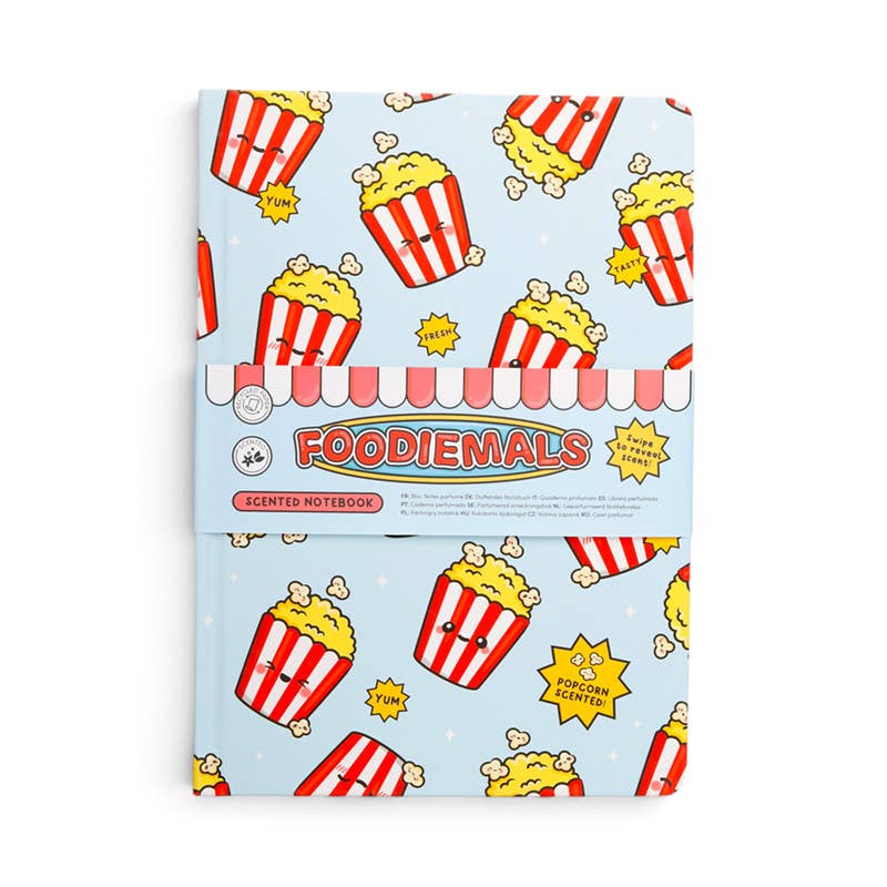 A Foodiemals scented notebook with a light blue cover decorated with a cartoon popcorn bucket pattern, wrapped in a pink and white striped paper band with the brand name 'FOODIEMALS' printed on it.