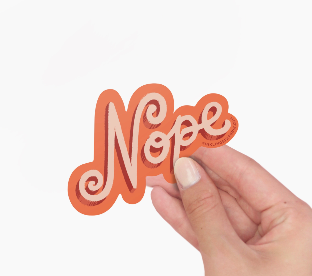 A hand holding a rectangular orange vinyl sticker with the word 'NOPE' written in a bold, cursive font.