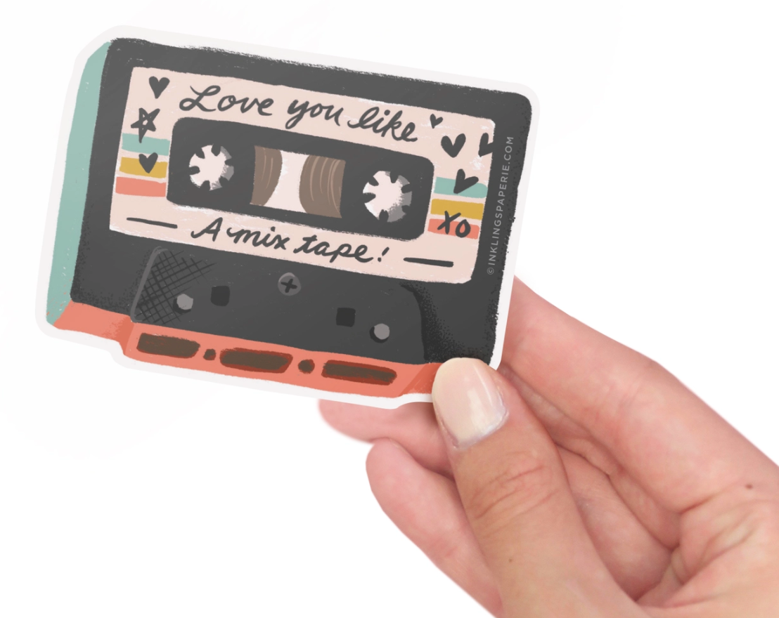 A vinyl sticker with a mix tape design, held between fingers with a nail polish visible.